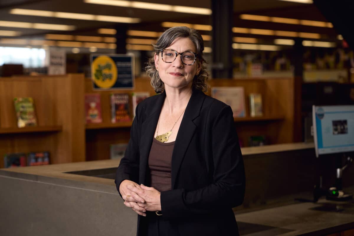 Alameda Post - A woman in a suit stands in the Alameda Main Library. 
