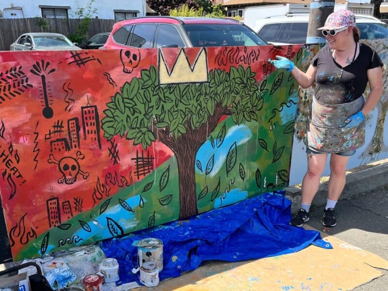 Alameda Post - a woman stands next to a mural with cans of paint