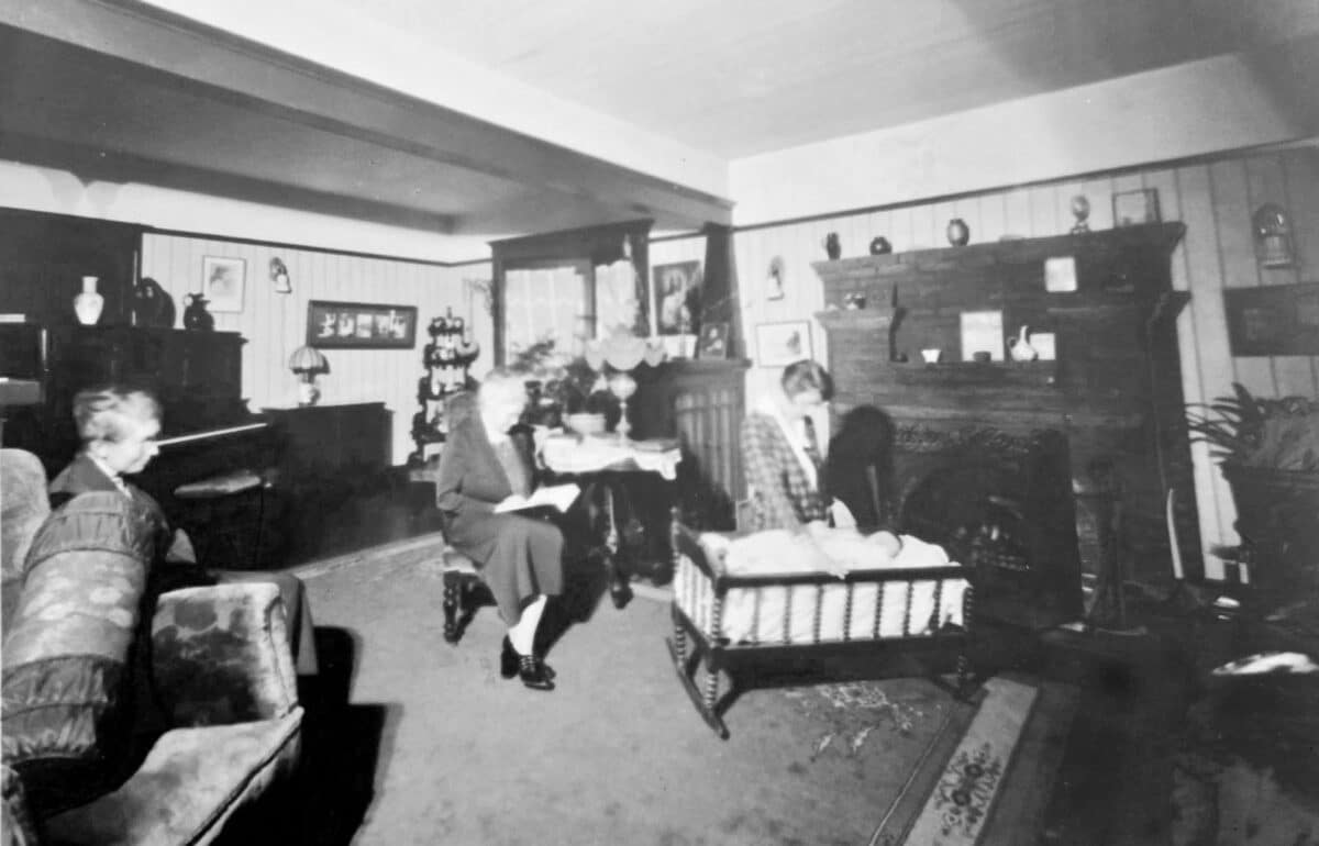 Alameda Post - An old black and white photo of three women enjoying a handsome living room, and one small baby laying in a rocking cradle.
