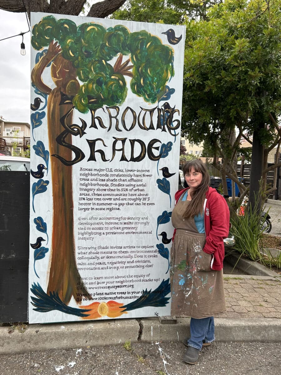 Alameda Post - An artist stands next to a mural of a tree that says Throwing Shade with text.