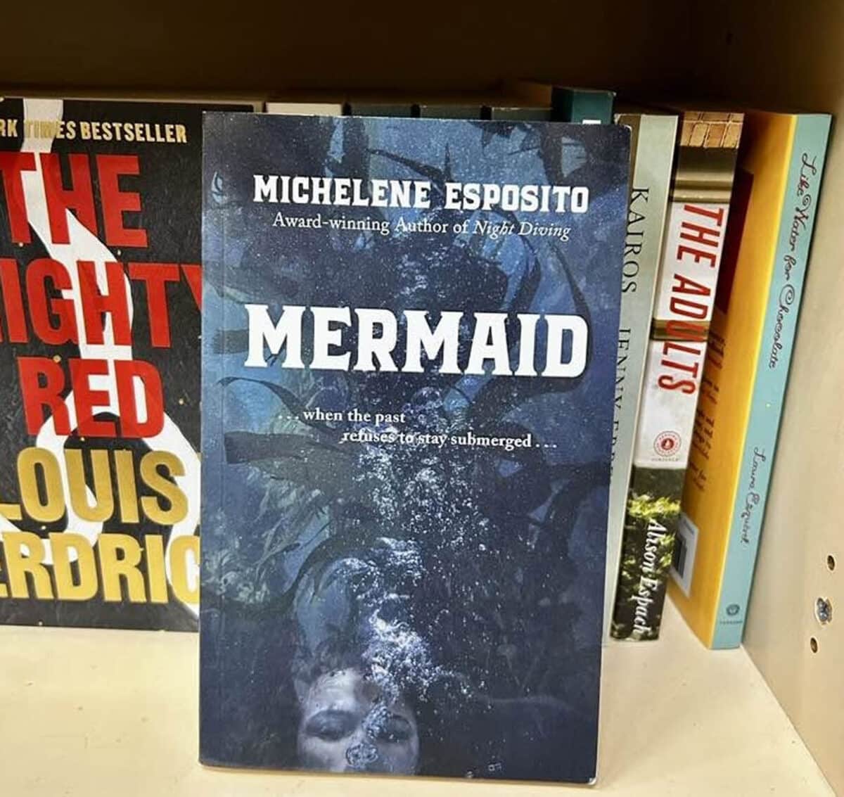 Alameda Post - The cover of the novel Mermaid. It shows a woman with bubbles coming up from her mouth against a watery background of kelp. 