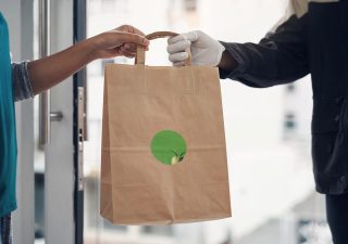 Alameda Post - a delivery driver hands food to a waiting person. Neither of their faces are visible.