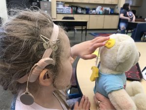 Alameda Post - a child with a cochlear implant adjusts the cochlear implant transmitter on a teddy bear designed by Fab Lab