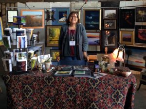 Alameda Post - Lisa Haderlie Baker stands at a table surrounded by art