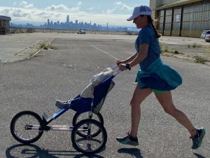 Alameda Post - a mom running with her baby in a stroller at Alameda Point with SF in the background