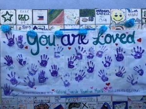 Alameda Post - A handmade poster with handprints that says "You are loved" and has the national suicide prevention phone number.