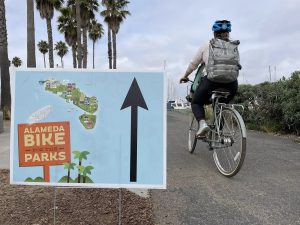 Alameda Post - a bicycle rider goes past a sign for Alameda Bike for the Parks