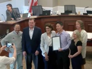 Alameda Post - A screen capture of City Council standing around City Attorney Yibin Shen who holds some kind of award or acknowledgement.